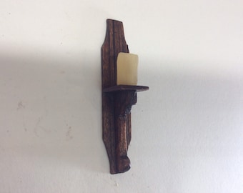 May include: A wooden wall-mounted candle holder with a single candle. The holder is dark brown with a carved design and a small shelf for the candle.