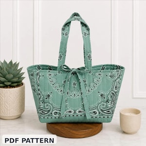 May include: A quilted tote bag in a teal paisley pattern with matching handles and a bow closure. The bag is sitting on a wooden stand. The text "PDF PATTERN" is at the bottom of the image.