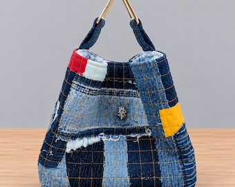 May include: A quilted denim handbag featuring a patchwork design of various blue fabric shades, accented with a bright yellow square patch and a red top trim. The bag includes a triangular gold-tone metal handle and a small silver star emblem.