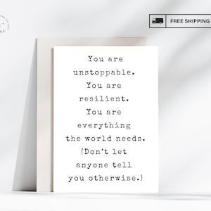 May include: A white greeting card with black typewriter-style text that reads: You are unstoppable. You are resilient. You are everything the world needs. (Don't let anyone tell you otherwise.) The card is positioned vertically against a plain background.