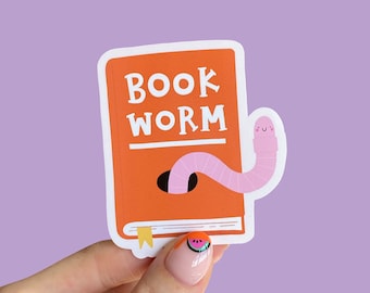 Peut inclure: Un autocollant orange avec les mots "Book Worm" en texte blanc. Un ver rose avec un visage souriant sort du livre.