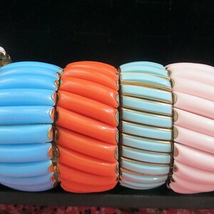 May include: A collection of six stretch bracelets featuring smooth, rectangular resin segments in light pink, sky blue, orange, turquoise, pale pink, and royal blue, each separated by thin gold-toned metal spacers arranged in a horizontal row.