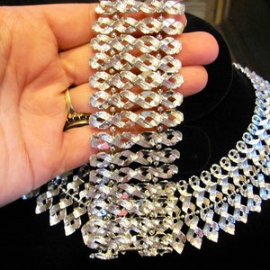 May include: A silver tone necklace and bracelet set with a geometric design. The necklace is a choker style and the bracelet is a wide cuff.