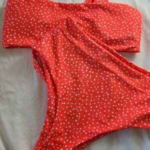 May include: A red and white polka dot bikini with adjustable straps. The top is a bandeau style and the bottom is a high-waisted style.