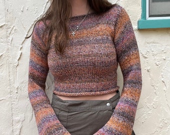 Puede incluir: Un suéter de punto de manga larga, corto y multicolor, con un corte holgado y mangas acampanadas. El suéter está hecho de una tela suave y de punto y tiene un estilo relajado y casual.