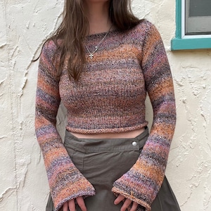 May include: A multi-coloured, long-sleeved, cropped sweater with a loose fit and bell sleeves. The sweater is made of a soft, knitted fabric and has a relaxed, casual style.