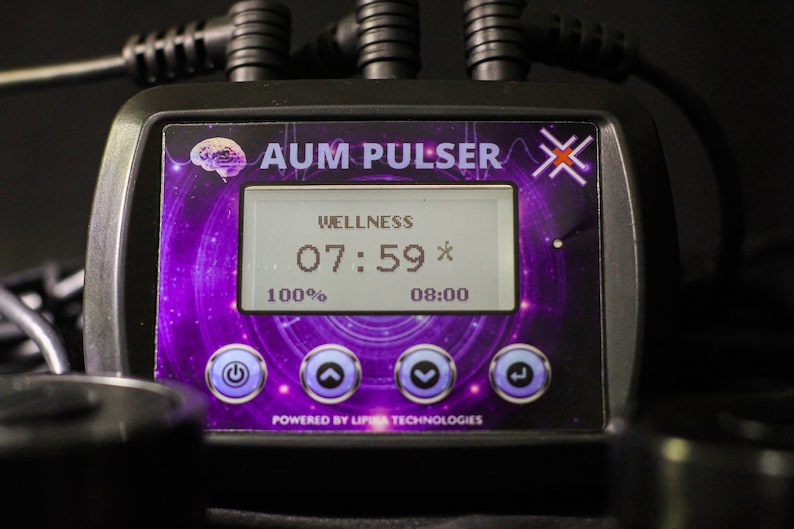 May include: A black device with a purple and white screen displaying "WELLNESS 07:59* 100% 08:00" and the text "AUM PULSER X" above the screen. The device has four buttons: power, up arrow, down arrow, and a right arrow.