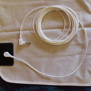 May include: A white heating pad with a white cord and a black control unit. The heating pad is on a white fabric surface.