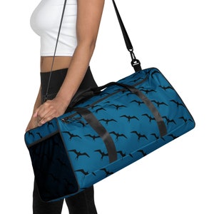 May include: A blue travel duffel bag with black straps and a black and white bird pattern. The bag has a zipper closure and a mesh pocket on the side.