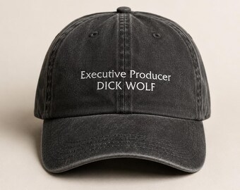 May include: A black baseball cap with the text "Executive Producer DICK WOLF" in white. The cap has a curved brim and an adjustable strap at the back. The hat is made of a soft, worn material.