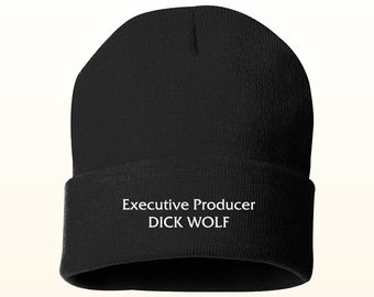 May include: A black beanie hat with a folded brim. The text "Executive Producer DICK WOLF" is printed in white on the brim. The hat is made of a soft, knitted material.