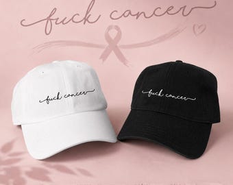 May include: Two baseball caps, one white and one black, are displayed. Each cap has the phrase "fuck cancer" embroidered in a cursive font. The background is a soft pink with a pink ribbon and the same phrase in a larger font.