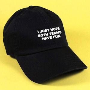 May include: A black baseball cap with white text that reads "I just hope both teams have fun".