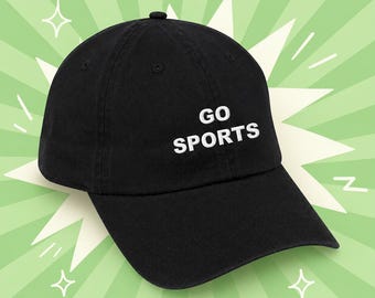 May include: Black baseball cap with the words "GO SPORTS" in white block letters. The cap has a curved brim and a small button on top. The background is a light green with white starburst and star shapes.