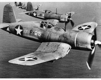 Op de afbeelding: Een zwart-witfoto van een formatie van vier US Navy Vought F4U Corsair-jager vliegtuigen in de lucht. Het vliegtuig op de voorgrond is gelabeld "F-25" en heeft een witte ster op de romp en vleugel.