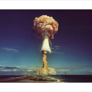 May include: A large mushroom cloud rises from the ocean, with a bright orange and white color. The cloud is surrounded by a blue sky and white clouds.
