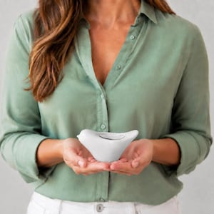 Peut inclure: Une petite figurine d'oiseau en céramique blanche, lisse et au design stylisé. L'objet présente un corps arrondi, un bec pointu et une petite indentation peu profonde sur le dos, le tout dans une finition blanche unie et épurée.