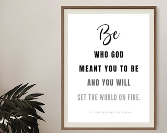 May include: A black and white inspirational quote print with a wooden frame. The quote reads "Be who God meant you to be and you will set the world on fire." The quote is attributed to St. Catherine of Siena.