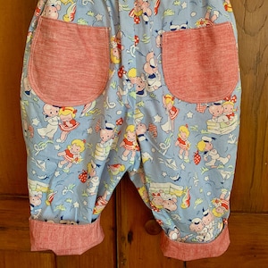 May include: Blue and red children's pants with a sailor and girl print. The pants have red pockets and red cuffs.
