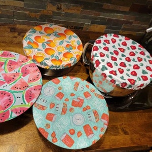 May include: Four reusable silicone bowl covers with different fruit designs. The covers are in a variety of colors, including pink, green, red, and orange. The covers are on a wooden surface.