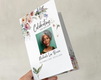May include: A memorial program featuring a photograph of a woman with grey hair, set against a green backdrop. The text reads "Celebrating the Life of Michaela Lee Brown" with dates. Floral watercolour designs in pink, purple, and green decorate the borders.