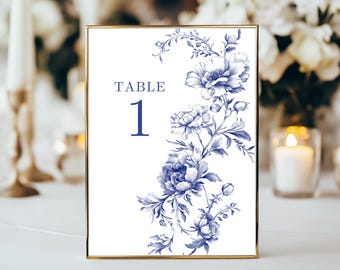 May include: A white table number card with a gold frame. The card features a blue floral design and the text "TABLE 1" printed in blue.