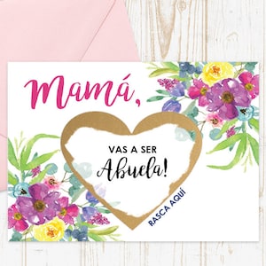 May include: A white card with a pink floral design and gold heart. The card says "Mamá, Vas a ser Abuela!" and "Rasca Aquí" in Spanish. The card is a scratch-off card to reveal the message.