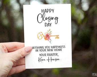 Può includere: Un biglietto bianco con il testo "HAPPY Closing DAY" e una chiave dorata con dettagli floreali. Il testo "WISHING YOU HAPPINESS IN YOUR NEW HOME YOUR REALTOR, Kara Hanson" è anche sul biglietto.