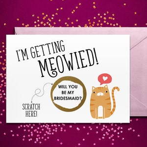 May include: A white greeting card with the black text I'M GETTING MEOWIED! and a gold scratch-off circle containing the text WILL YOU BE MY BRIDESMAID? A cartoon orange tabby cat with a red speech bubble and white heart is printed on the card.