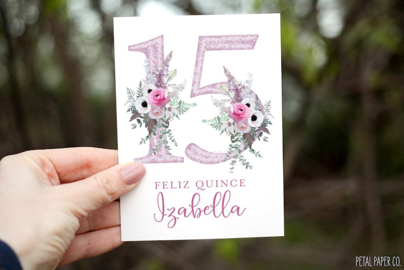 May include: A pink and white floral design with the number 15 in the center. The text "Feliz Quince Izabella" is below the number.