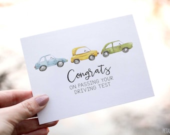 May include: A white card with a blue, yellow, and green car illustration. The text on the card reads "Congrats on passing your driving test."