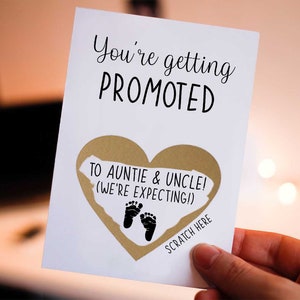 May include: A white card with the text "You're getting promoted to auntie & uncle! (We're expecting!)" and a gold heart with black footprints. The text "Scratch here" is below the heart.