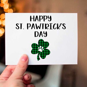 May include: A white card with the text "Happy St. Pawtrick's Day" and a green and black shamrock with a white paw print in the center.