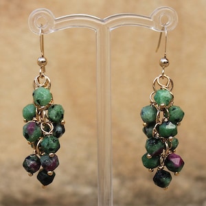 May include: Gold earrings featuring a cluster of green and pink gemstones. The earrings are drop earrings with a delicate chain design.
