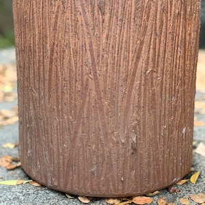 May include: A brown ceramic planter with a wood-like texture. The planter is cylindrical and has a smooth, rounded bottom.