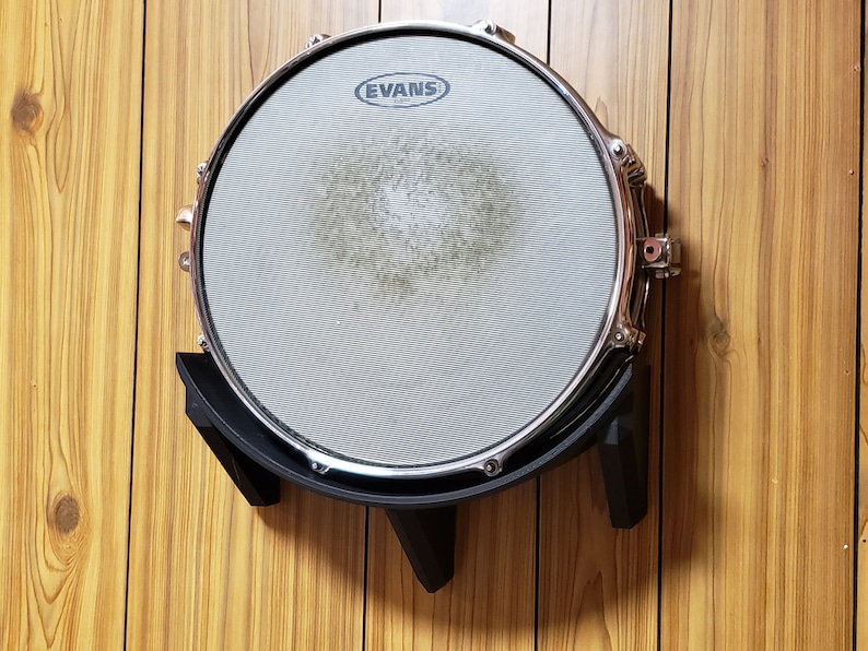 May include: A black drum rack with a silver snare drum mounted on it. The snare drum has an Evans logo on the head.
