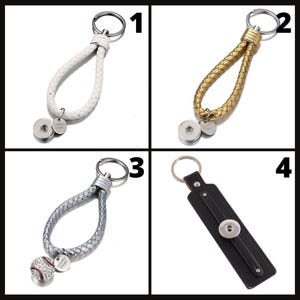 May include: Four keychains with metal key rings. The first is white braided leather, the second is gold braided leather, the third is silver braided leather with a baseball charm, and the fourth is black leather.