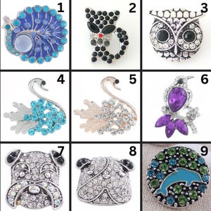 May include: A collection of nine decorative brooches. The brooches feature various designs, including a peacock, cat, owl, swan, bird, and dog. Each brooch is embellished with rhinestones in various colors, such as blue, black, silver, and purple.