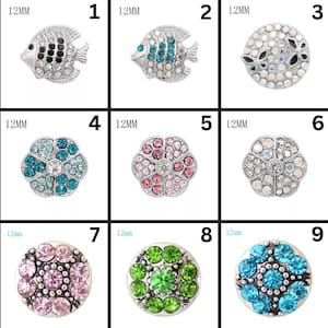 May include: A collection of nine decorative snap buttons. The buttons feature various designs, including fish, floral patterns, and circular arrangements of colorful rhinestones. Each button is approximately 12mm in diameter, with a silver-tone metal base.