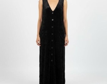 Puede incluir: Un vestido largo sin mangas de terciopelo negro con un escote en V profundo, cierre frontal de botones en toda la longitud con botones negros a juego y dos grandes bolsillos de parche en la parte delantera. Corte recto hasta el suelo.