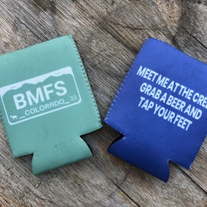May include: Two beverage insulators, one green with the text "BMFS_COLORADO_33" and the other blue with the text "MEET ME AT THE CREEK GRAB A BEER AND TAP YOUR FEET"