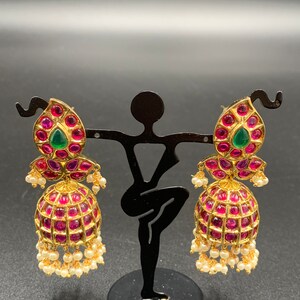 Pode incluir: Um par de brincos de ouro com pedras preciosas rosa e verdes. Os brincos têm a forma de uma lágrima e têm uma bola pendurada na parte inferior.