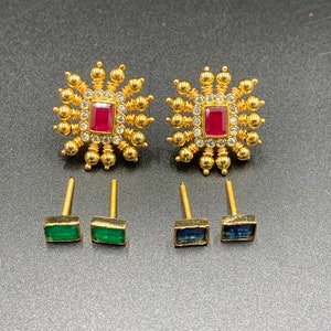 May include: A set of gold earrings with a starburst design and red and blue gemstones. The earrings are on a black surface.