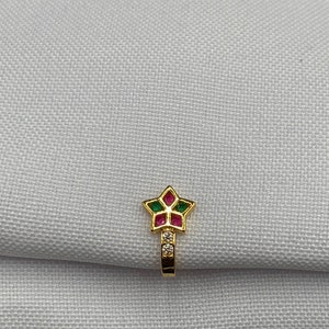 May include: Gold nose ring with a star-shaped design. The star is decorated with pink and green gemstones and clear rhinestones.