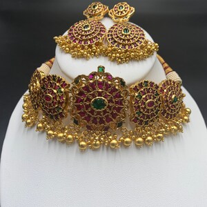 Pode incluir: Um colar choker de ouro com um design floral e pedras preciosas rosa e verdes. O colar é combinado com brincos correspondentes.