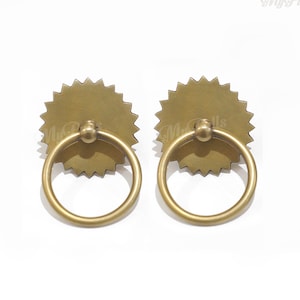 以下が含まれることがあります： 星形のデザインとリングハンドルが付いた真鍮製のドアノブ2個。ノブは暖色系のゴールドです。