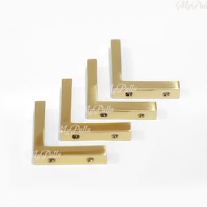 May include: Four gold-colored metal corner brackets, arranged in a staggered pattern, with two screw holes on each bracket.