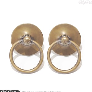May include: Two antique brass ring cabinet pulls with a round base. The pulls have a smooth, polished finish.