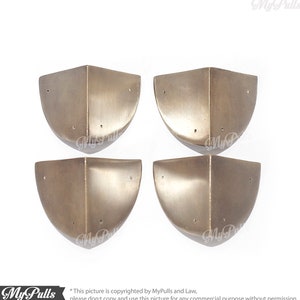 May include: Four corner protectors made of metal in a silver finish. The protectors are shaped like a quarter circle and have a smooth, slightly textured surface.