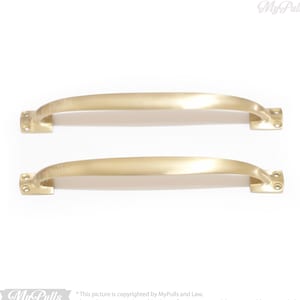 Może przedstawiać: Dwa złote uchwyty do drzwi szafki o zakrzywionym kształcie. Uchwyty są wykonane z metalu i mają gładkie, polerowane wykończenie.